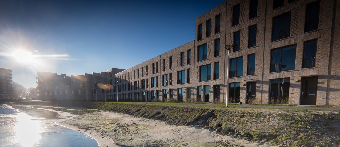 Het project Poortmeesters, een lange rij gevels langs het water, met daarin een donkerblauwe poort naar de binnenplaats.